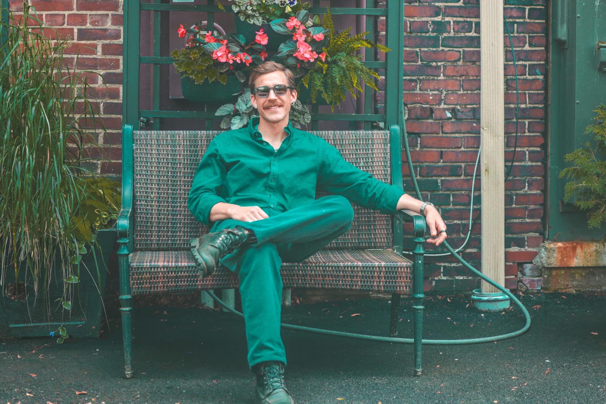 Man in a green jumpsuit relaxing on a bench beside a flower-covered wall