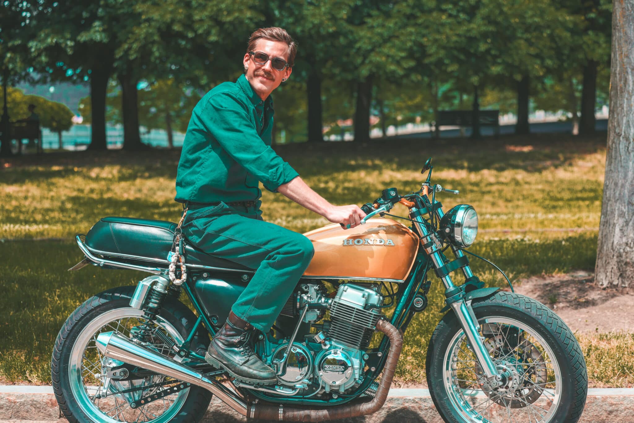 Man in a green jumpsuit riding a vintage motorcycle near a Finger Lakes park