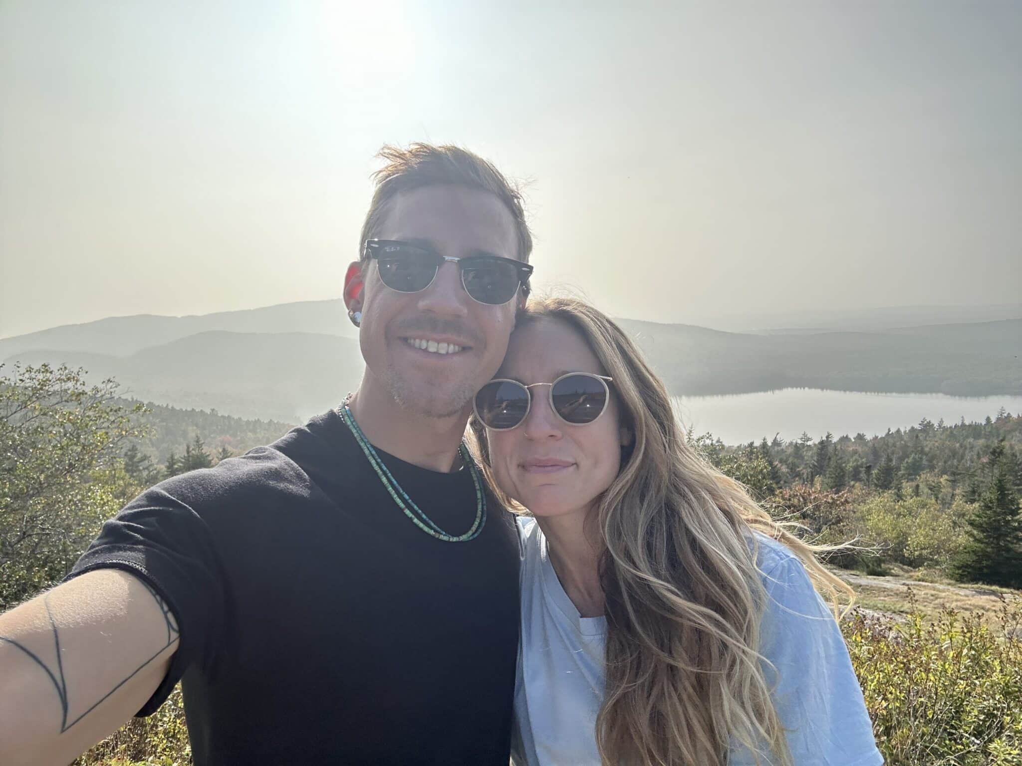 Couple smiling for a selfie on a hilltop overlooking the Finger Lakes