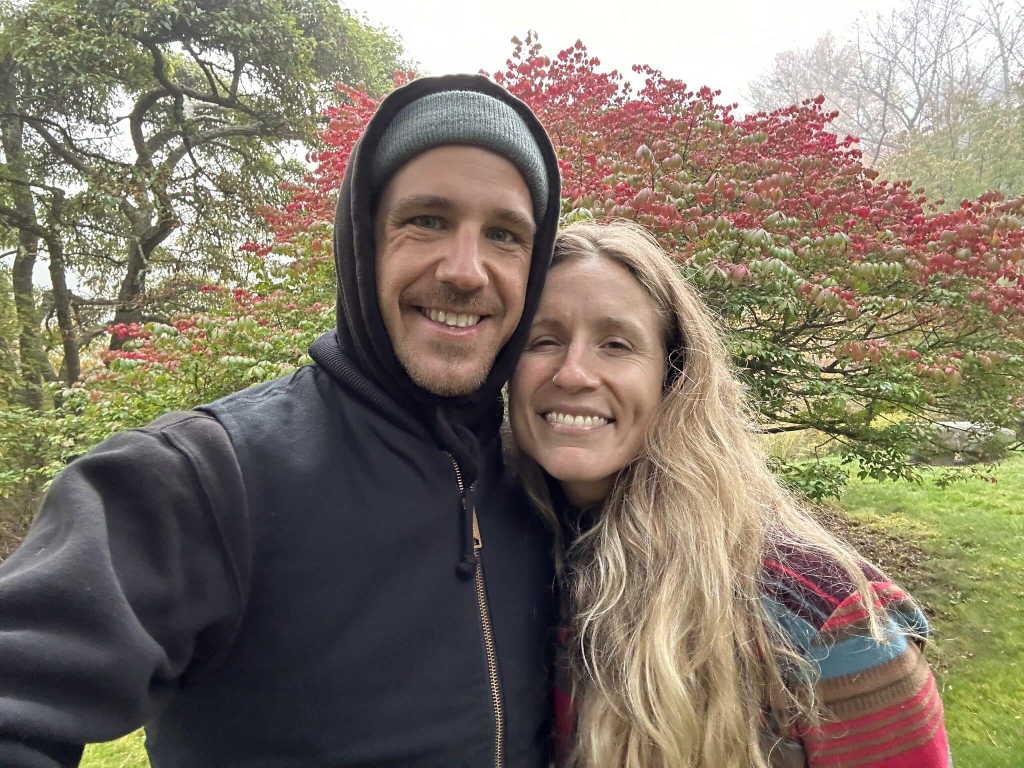 Couple smiling together in a garden beside a red-leafed Japanese maple