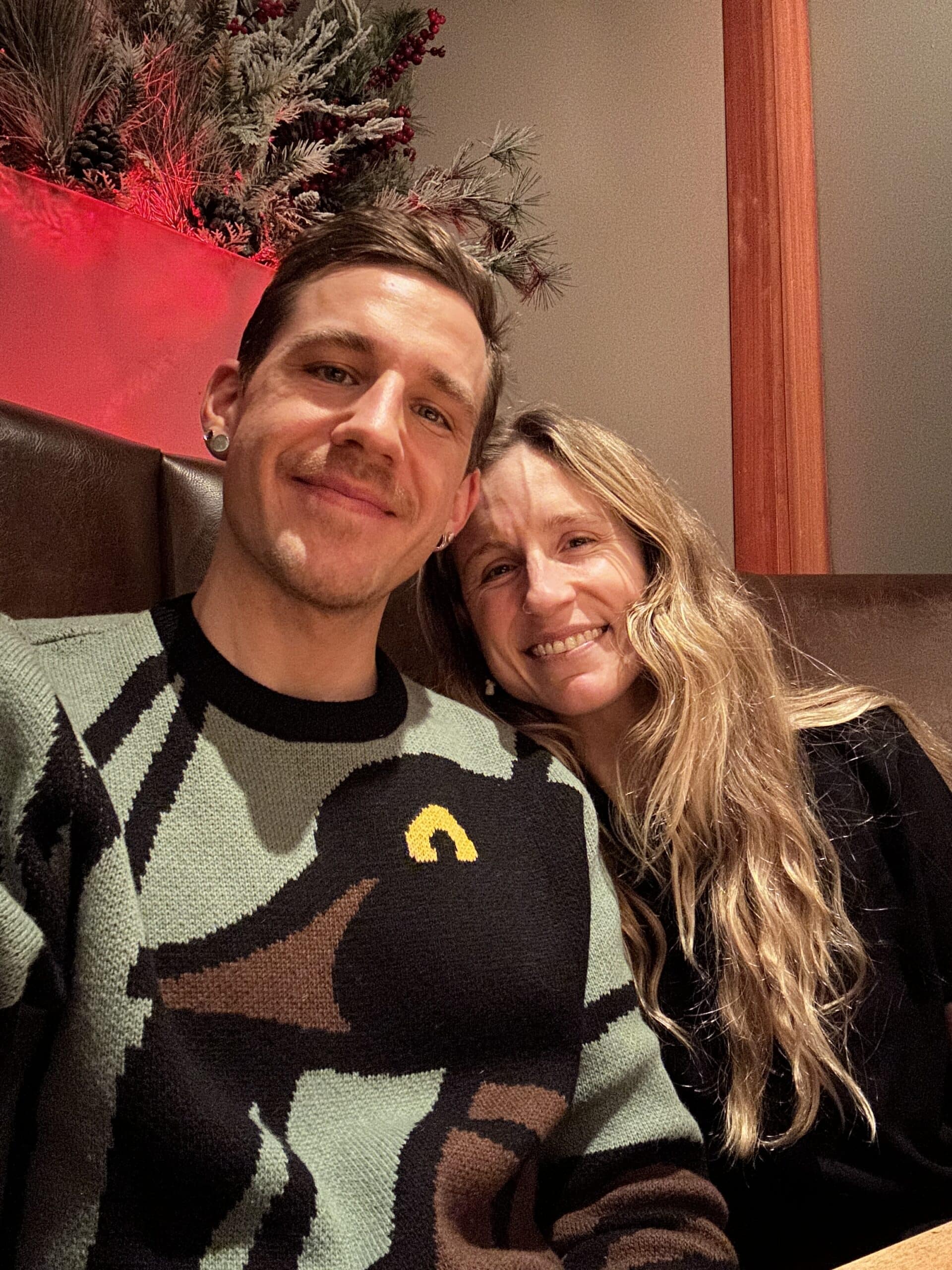 Couple smiling closely together in sweaters at an indoor gathering