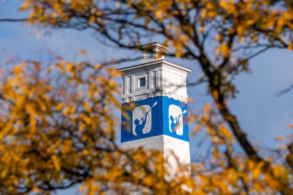 Blue and white water tower peeking through autumn treetops in Corning