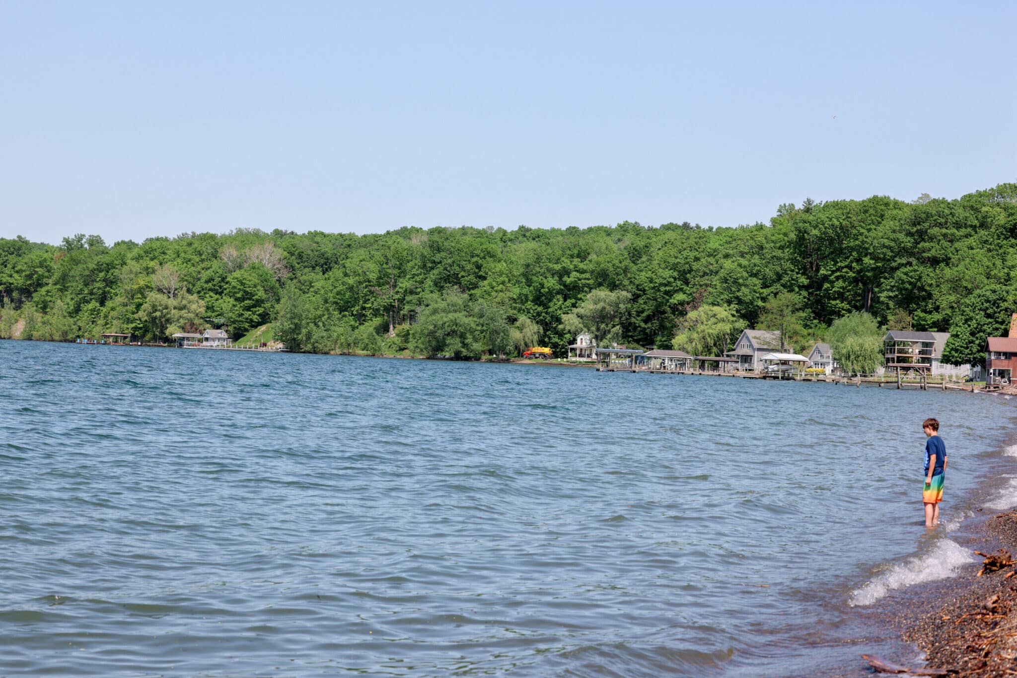 Child playing at the edge of a Finger Lake with cottages along the far shore